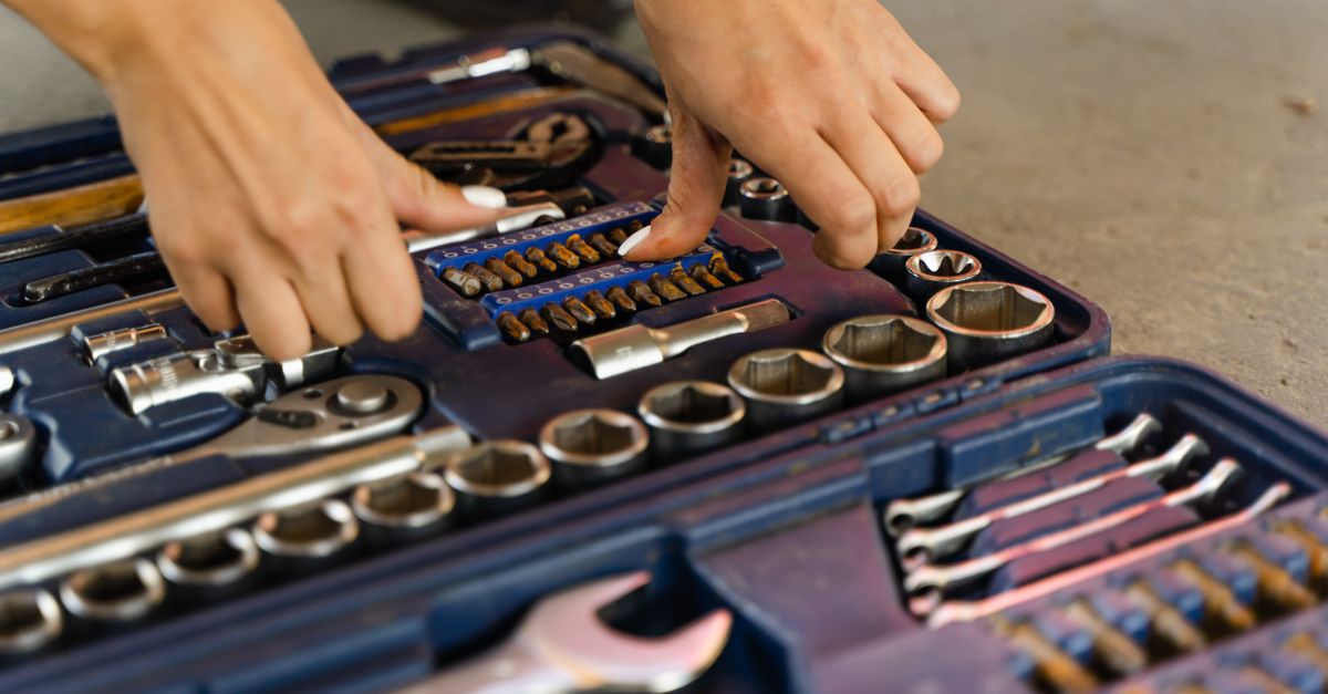 Hands selecting tools from a well-organized toolbox on a concrete surface.